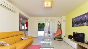 A living room with a yellow sofa, a glass coffee table, a hanging chair, a TV, and a cityscape painting. - House 2447/252732 (Istria - Banjole), 1000m from the beach (Banjole)