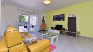 A living room with a yellow sofa, a glass coffee table, a hanging chair, a flat-screen TV, and a painting on the wall. - House 2447/252732 (Istria - Banjole), 1000m from the beach (Banjole)