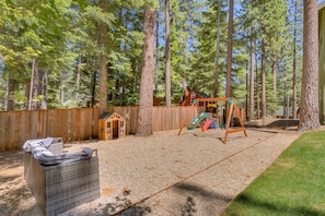 A backyard with a swing set, a wooden playhouse, and a wicker chair. - Mountain Retreat, Theater Room, Hot Tub, Pac-Man Arcade & Stone Fireplace: Sugar Pine Lodge (South Lake Tahoe)