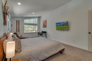 A bedroom with a large bed, a desk, a chair, a TV, and a window with a view of trees. - Mountain Retreat, Theater Room, Hot Tub, Pac-Man Arcade & Stone Fireplace: Sugar Pine Lodge (South Lake Tahoe)