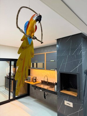 A modern kitchen with a black marble backsplash, a built-in oven, and a hanging parrot sculpture. - Casa Brisa Baiana, leisure area, 250 meters from the beach. (Prado)
