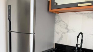 Eine Küche mit einem Edelstahl-Kühlschrank, einer schwarzen Arbeitsplatte, einem Spülbecken mit Armatur und Holzschränken.