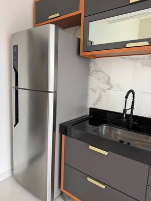 A kitchen with a stainless steel refrigerator, a black countertop, a sink with a faucet, and wooden cabinets. - Casa Brisa Baiana, leisure area, 250 meters from the beach. (Prado)