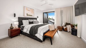 Ein modernes Schlafzimmer mit einem großen Bett, Nachttischen, einer Bank, einem Deckenventilator und Blick ins Freie.