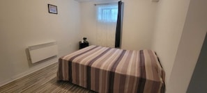 A small, single-bed room with a radiator, a window with curtains, and a framed picture on the wall.