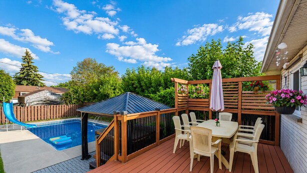 Eine Holzterrasse mit Pool, überdachter Sitzbereich und Tisch mit Stühlen.
