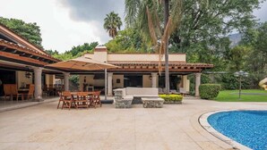 A poolside area with outdoor furniture, a covered seating area, and a view of the surrounding greenery.
