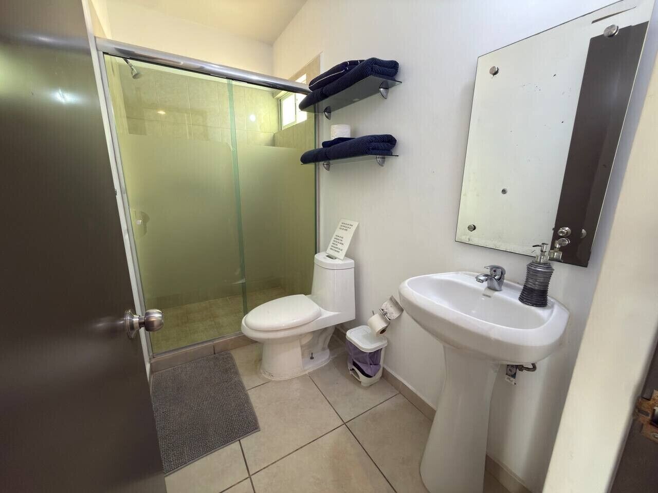 A bathroom with a glass shower enclosure, a toilet, a sink, and a mirror.
