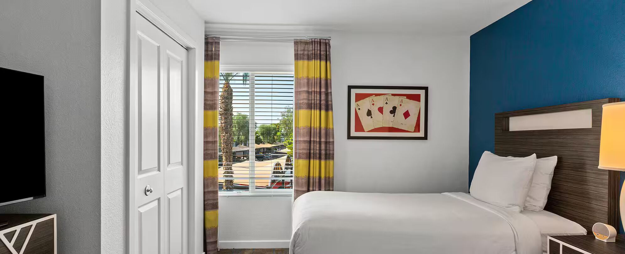 Habitación de hotel con cama, televisor, un cuadro y vistas al exterior.