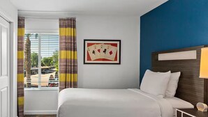 Ein Hotelzimmer mit Bett, Fernseher, einem gerahmten Bild und Blick nach draußen.