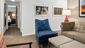 Ein Hotelzimmer mit blauem Sessel, beiger Couch, roter Lampe und gerahmten Bildern an der Wand.