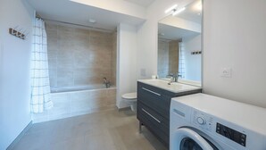 A modern bathroom with a bathtub, toilet, vanity, and a washing machine. - Le Nid des Bisson - Welkeys (Dives-sur-Mer)