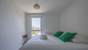 A bedroom with a bed, a window, and a view of buildings outside. - Le Nid des Bisson - Welkeys (Dives-sur-Mer)