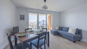 A modern living room with a dining area, a grey sofa, and a dining table set with plates and glasses. - Le Nid des Bisson - Welkeys (Dives-sur-Mer)