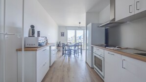 A modern kitchen with white cabinets, a wooden countertop, and a dining area with chairs. - Le Nid des Bisson - Welkeys (Dives-sur-Mer)