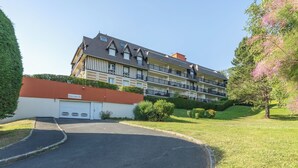 Un immeuble résidentiel à plusieurs étages, doté d’un garage, entouré de pelouses et d’arbres bien entretenus.