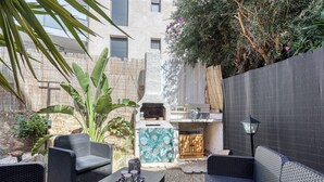 A patio area with wicker furniture, a grill, and a decorative wall. - Le Jardin du Littoral - Welkeys (Bandol)
