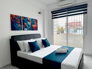 Moderni hotellihuone, jossa on sänky, näkymä ikkunasta ja kaksi seinälle asennettua taideteosta.