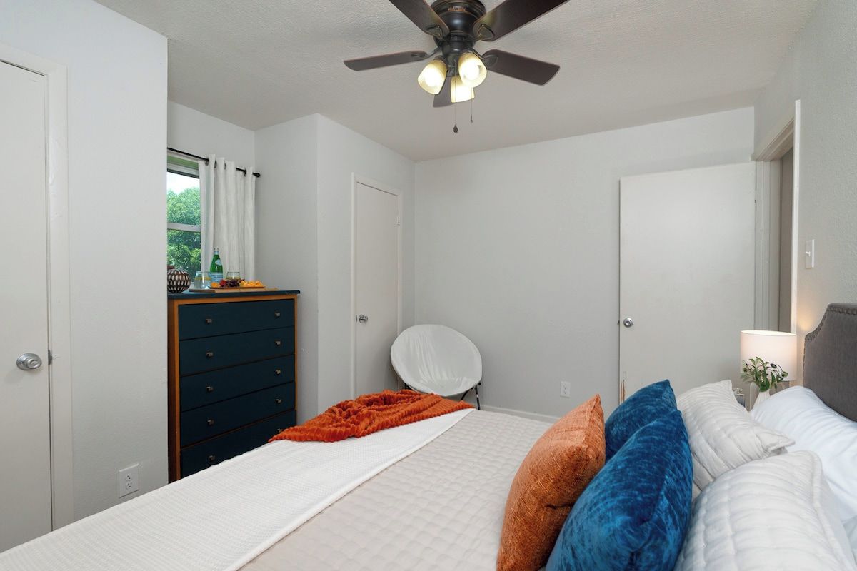 Un dormitorio con cama, ventilador de techo, cómoda y ventana con cortinas.