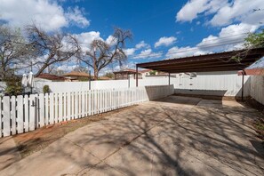 A backyard with a white picket fence, a covered patio area, and a clear blue sky. - Ten33 | Luxe Sayles District Experience, King Bed! (Abilene)