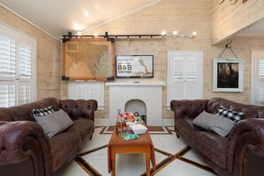 A cozy living room with two leather sofas, a wooden coffee table, and a fireplace. - Ten33 | Luxe Sayles District Experience, King Bed! (Abilene)