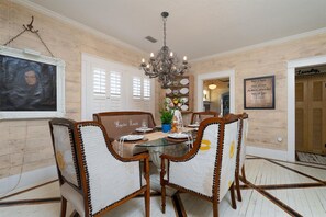 A dining area with a glass table, wooden chairs, a chandelier, and a wall-mounted picture. - Ten33 | Luxe Sayles District Experience, King Bed! (Abilene)