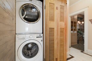 A laundry area with stacked washing machines and a wooden door leading to a kitchen area. - Ten33 | Luxe Sayles District Experience, King Bed! (Abilene)