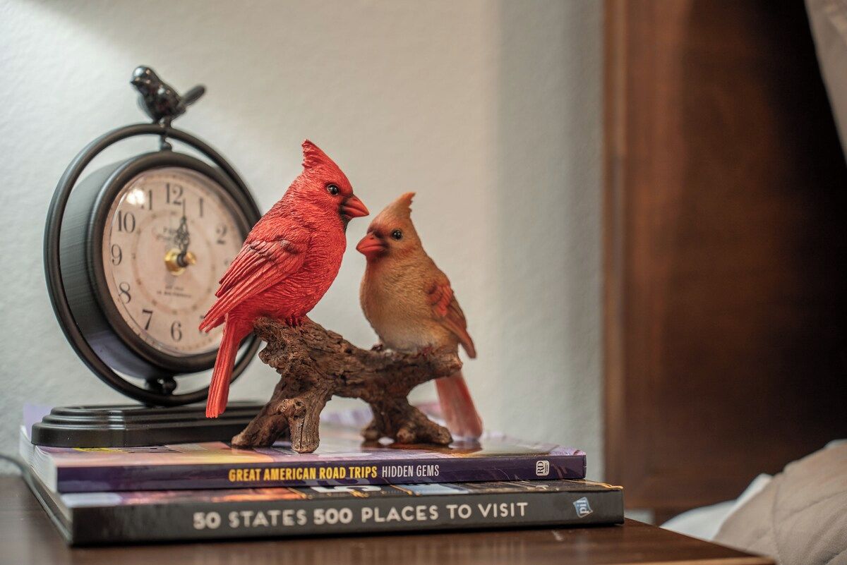 A clock and two bird figurines on a table with books.