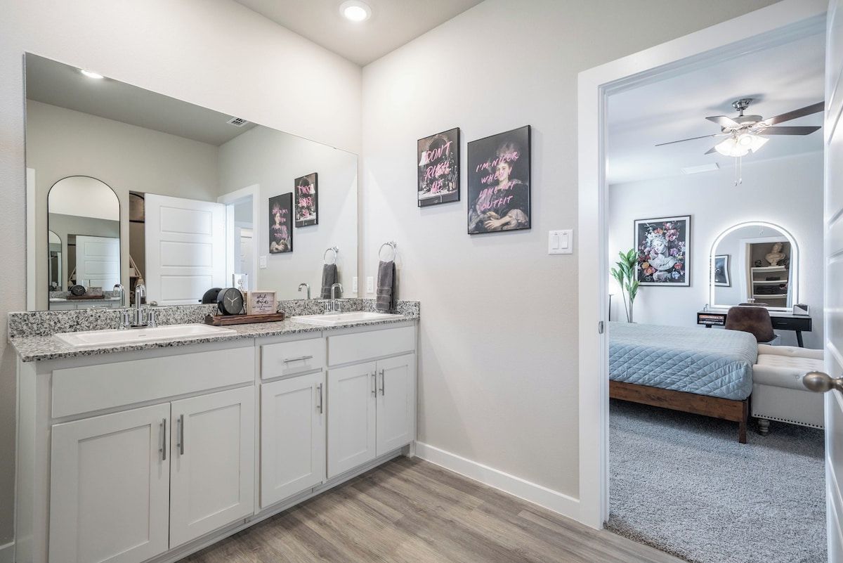 A modern bathroom with a large mirror, white cabinets, and a vanity with a sink.