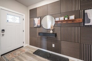A modern hallway with a white door, a mirror, a shelf with decorative items, and a patterned wall. - 5-Bedroom Themed Retreat - The Providence (Abilene)