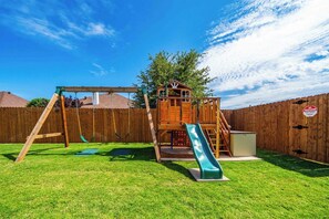 A backyard with a wooden playset including a slide, swing set, and climbing structure. - 5-Bedroom Themed Retreat - The Providence (Abilene)