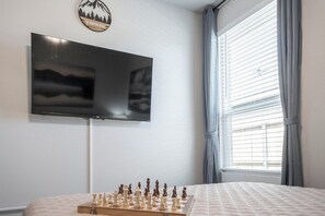 A bedroom with a bed, a television mounted on the wall, and a chessboard on the floor.