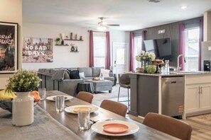 Cozinha moderna com área de refeições, sofás cinzas e televisão de tela plana.