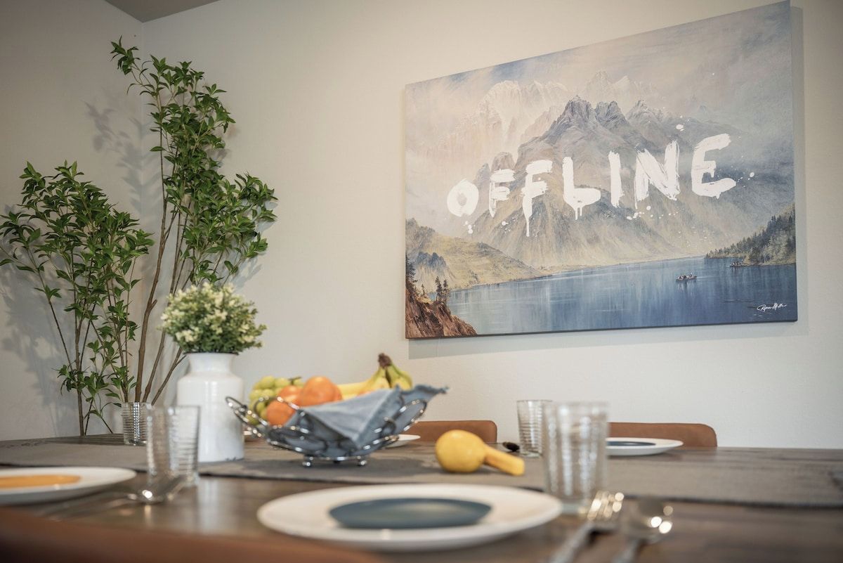 Ein Essbereich mit einem Tisch für zwei Personen, einem Gemälde einer Berglandschaft und einer Vase mit Blumen. Auf der Wand ist das Wort 'OFFLINE' zu sehen.