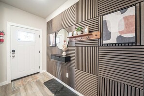 Um corredor com parede de painel de madeira, mesa consola preta com espelho e prateleira com objetos decorativos.
