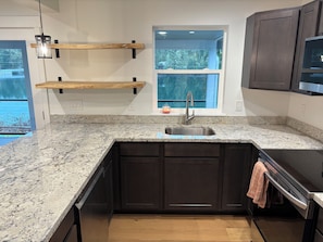 A kitchen with granite countertops, dark cabinetry, a stainless steel sink, wooden shelves, and a window with a view. - Charming 3-bedroom house in enjoyable Gig Harbor with AC (Gig Harbor)