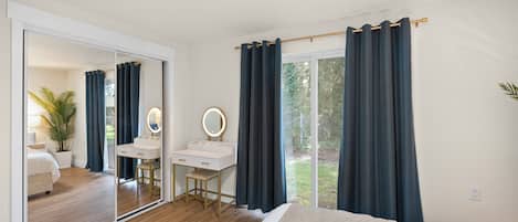 Una camera da letto con un letto, una scrivania con uno specchio, un comò e una porta vetrata scorrevole che dà su un balcone.