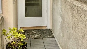 Une porte blanche avec un panneau de verre, une rambarde en métal et un pot de fleurs posé sur le sol.