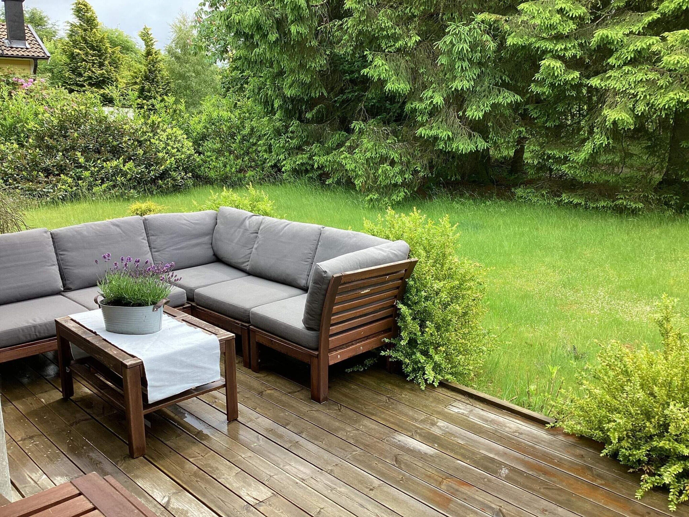 A wooden deck with a gray outdoor sofa, a small table with a white tablecloth, and a potted lavender plant.