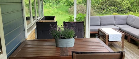 Une terrasse extérieure avec une table et des chaises en bois, un canapé gris et une plante en pot.