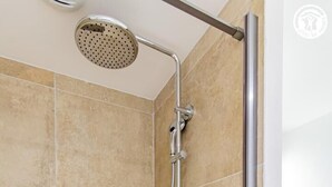 Een douche met een handdouche, een bedieningspaneel aan de muur en een klein plankje.