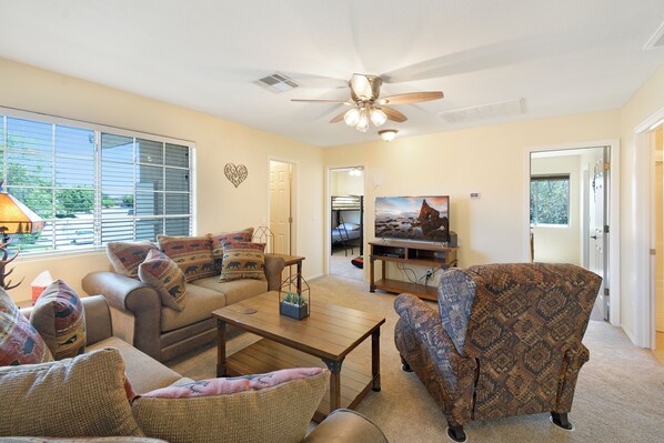 A living room with a ceiling fan, a sofa, a patterned armchair, a coffee table, and a television.