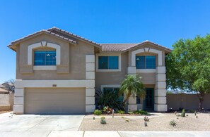 A two-story house with a garage, a landscaped front yard with cacti and a palm tree, and a clear blue sky.