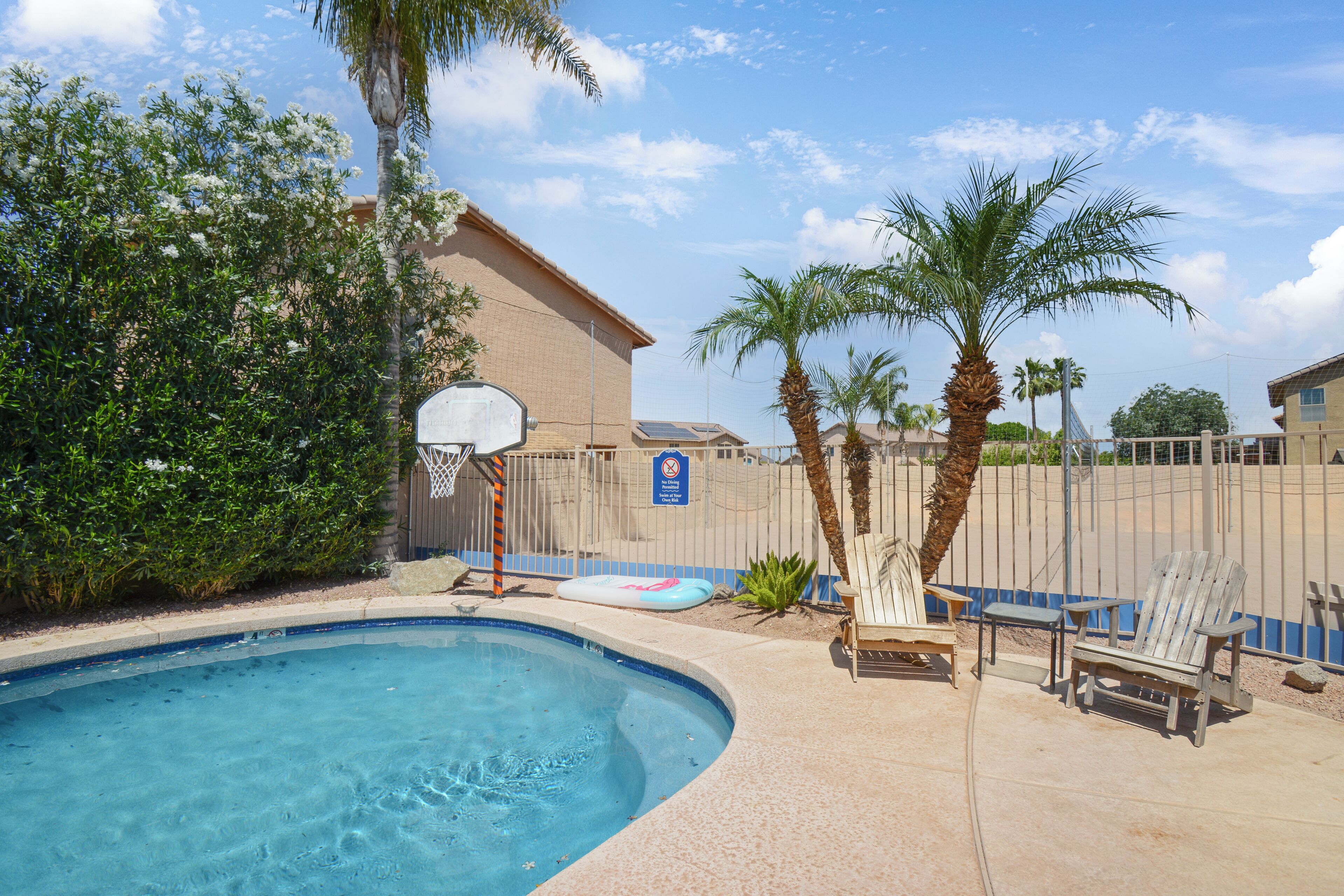 A swimming pool with a basketball hoop, palm trees, and a fence.