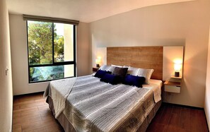 Une chambre avec une grande fenêtre, une tête de lit en bois, un lit avec de nombreux oreillers et des lampes de chevet.