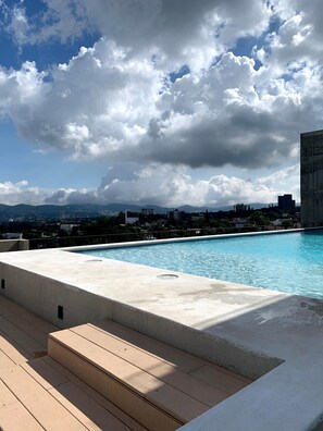 Une piscine sur le toit offrant une vue sur le paysage urbain et les montagnes au loin.