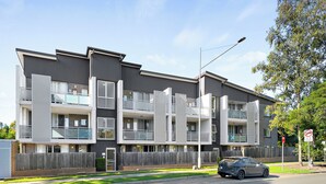 Un immeuble résidentiel à plusieurs étages, doté de balcons, avec une voiture garée devant et un panneau indiquant qu’il est interdit de se garer.