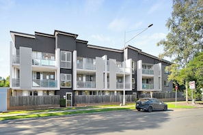 A multi-story residential building with balconies, a car parked in front, and a no parking sign.