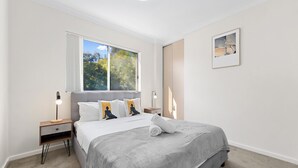 Une chambre à coucher avec un lit, des tables de chevet, une fenêtre et un tableau encadré au mur.