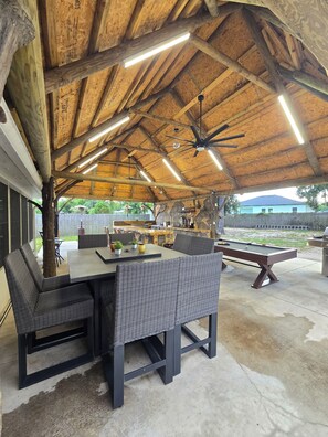 Eine überdachte Außenveranda mit Billardtisch, Korbmöbeln und Deckenventilator.